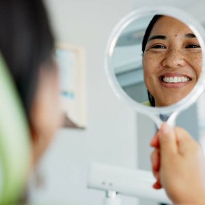 Woman smiling at reflection in handheld mirror