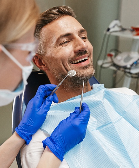 Dentist approaching man’s mouth with examination instruments