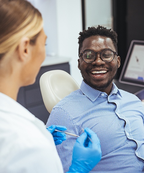 Man with glasses in dental chair smiling at dentist