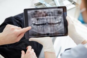 Dentist showing patient X-ray of teeth on a tablet.